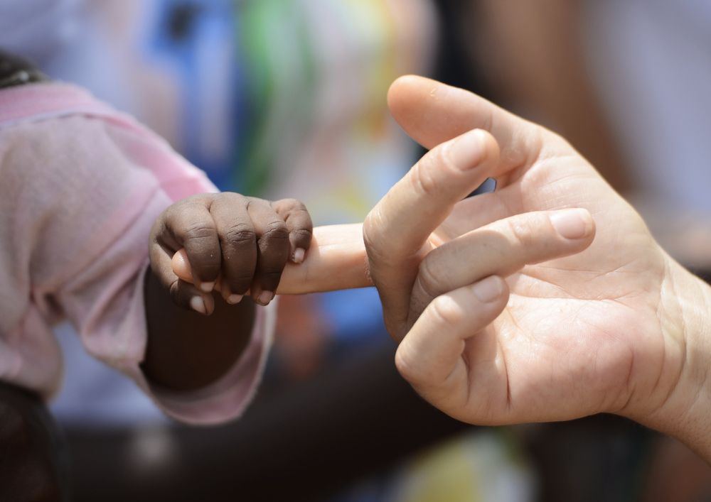 Turismo e sostenibilit&agrave;: la mano di un bambino nero stringe il dito di un bianco, sindrome del white savior 